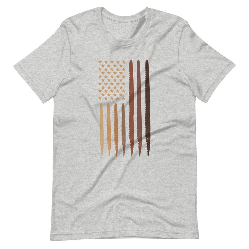 Op de afbeelding: Een heidekleurig T-shirt met een afbeelding van een Amerikaanse vlag. De vlag wordt weergegeven met een veld van witte sterren en rode en witte strepen. De strepen zijn vervangen door verschillende tinten bruin.