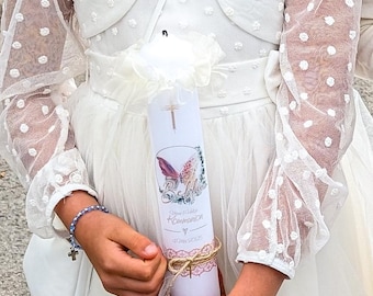 May include: A white communion candle with a butterfly design and the words "Belife Kommunion" in gold script. The candle is held by a person wearing a white dress with a dotted overlay and a matching bolero.