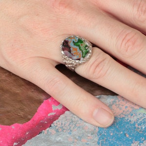 May include: A silver ring with a large oval-shaped gemstone. The gemstone is a mix of green, brown, and white colors.