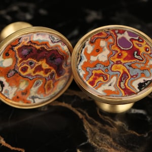 May include: Two round, gold-toned cufflinks with a colourful, abstract, agate-like design. The design features swirls of orange, red, white, blue, and black.