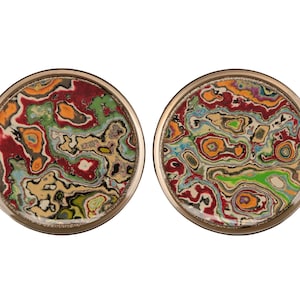 Può includere: Due sottobicchieri rotondi con bordo dorato, che presentano un motivo astratto colorato e vorticoso in tonalità di rosso, verde, giallo e blu.