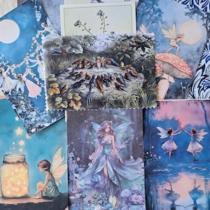 May include: A collection of rectangular cards featuring fairy illustrations. Designs include a fairy with a jar of glowing lights, a fairy in a flowing gown, two fairies dancing over water, a fairy on a mushroom, and a central card showing a fairy with birds.