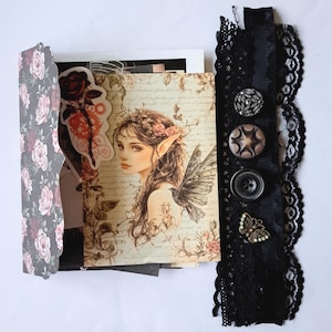 May include: A decorative scrapbook page featuring a fairy portrait with floral accents and a black lace ribbon. The fairy has long brown hair, pointed ears, and butterfly wings. The ribbon has decorative buttons and a butterfly charm.