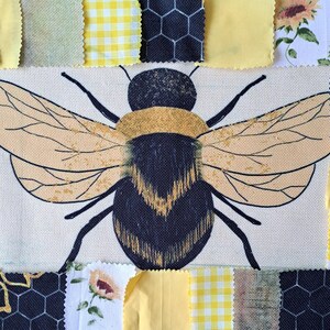 May include: A patchwork design with a central bumblebee illustration. The bee has tan wings and a black and yellow body, set against a white background. It's surrounded by fabric squares in yellow, black, and floral patterns.