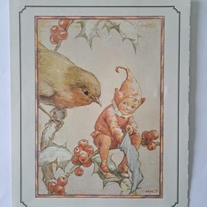 May include: A vintage-style illustration print featuring a brown robin perched on a holly branch with red berries and green leaves. Beside the bird, a small figure in a red cap and outfit holds a blue stocking. The initials M.W.T. appear at the bottom.