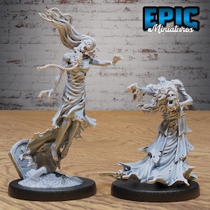 Könnte beinhalten: Zwei unbemalte, graue, Plastik-Miniaturfiguren von weiblichen Zombies, die lange Kleider tragen. Der Zombie links schwebt mit ausgestreckten Armen und einem Seil um den Hals. Der Zombie rechts steht mit fehlendem Kopf und ausgestreckten Armen. Die Figuren stehen auf schwarzen Sockeln mit einer grauen, strukturierten Oberfläche.