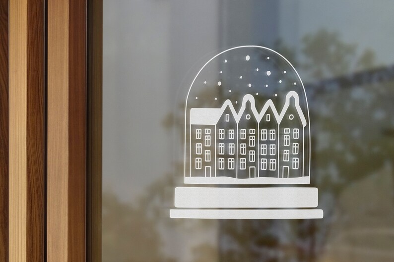 May include: A white silhouette of a snow globe with a row of houses inside. The snow globe is on a window with a wooden frame.
