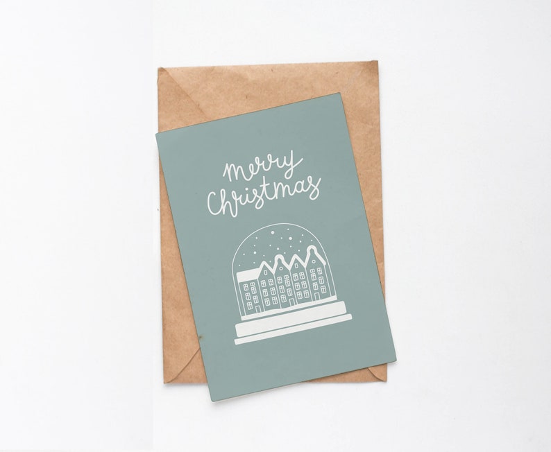 May include: A light blue Christmas card with the text "merry Christmas" in white cursive lettering. The card features a white illustration of a snow globe with a small town inside.