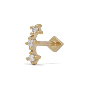 Puede incluir: Joyería corporal de oro con tres pequeños diamantes engastados en una línea curva. La joyería está diseñada para un piercing de cartílago.