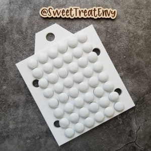 May include: White plastic mold with 50 round depressions for making candy or chocolate. The mold has a handle on the top and is designed for making round candies.