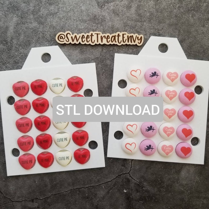 May include: Two white trays with heart-shaped candy moulds. The left tray has red candy moulds with the text "Cutie Pie" and "Be Mine". The right tray has pink and white candy moulds with a heart and cupid design. The text "STL DOWNLOAD" is printed in the centre of the image.