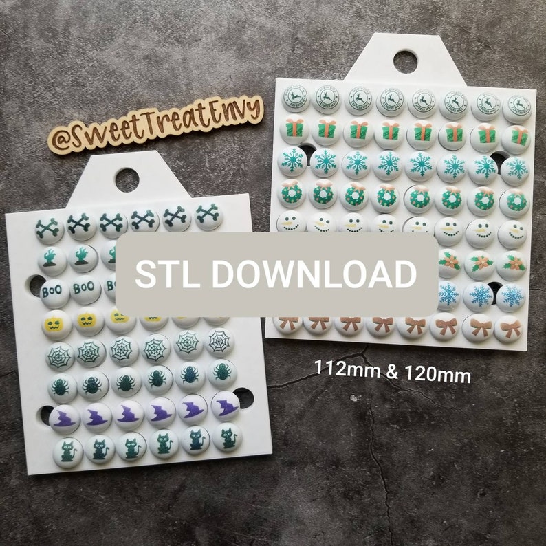 May include: Two white boards with different holiday themed buttons. The left board has Halloween themed buttons with images of ghosts, pumpkins, spiders, bats, and cats. The right board has Christmas themed buttons with images of presents, snowflakes, wreaths, snowmen, and bows. The boards are labeled "STL DOWNLOAD" and "112mm & 120mm".