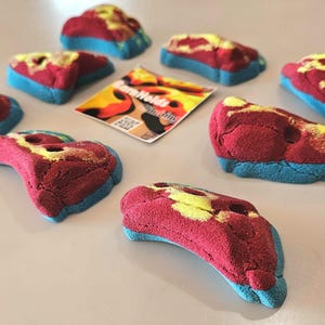 May include: A collection of colorful climbing holds in red, yellow, and blue. The holds are irregularly shaped with a textured surface. A small card with the text "ClimbHolds" is also present.