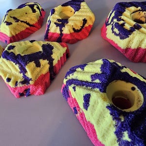 May include: Five colorful climbing holds with a yellow, pink, and purple color scheme. The holds are made of a textured material and have different shapes and sizes.