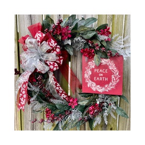 Cranberry and silver holiday wreath with sparkling eucalyptus leaves, burgundy flowers and berries. Wooden PEACE ON EARTH sign and big bow.