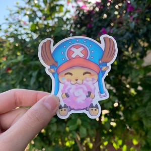 May include: A sticker featuring a cartoon character with a blue and white hat, brown antlers, and a pink and white cotton candy. The character is smiling and holding the cotton candy in its hands.
