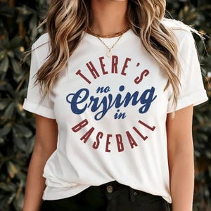 May include: White t-shirt with a red and blue circle graphic that says "There's no crying in baseball."