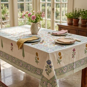 Può includere: Una tovaglia rettangolare con base color crema caratterizzata da un motivo floreale ripetuto nelle tonalità del verde, rosa, giallo e blu. Il bordo presenta una stampa botanica dettagliata, mentre il centro ha un motivo floreale sparso.