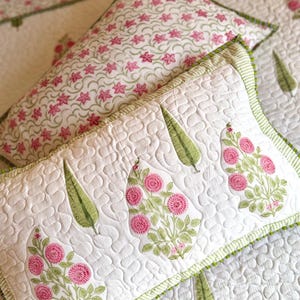 May include: Two rectangular quilted pillows featuring a white base with green and pink floral and leaf patterns. The front pillow displays pink circular flower clusters and green leaves, while the back pillow has a repeating pink star pattern.