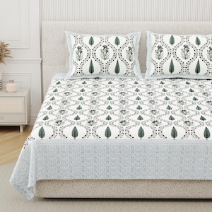 Può includere: Un lenzuolo bianco e due federe abbinate con un motivo ripetuto di alberi verde scuro e disegni floreali all'interno di una griglia nera. Il bordo inferiore del lenzuolo presenta una larga fascia con un motivo geometrico a griglia azzurro.