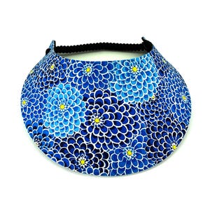 May include: A blue visor with a floral pattern. The visor features a repeating design of blue flowers with white outlines and yellow centers. The headband is black and elastic. The visor is designed to shield the eyes from the sun.