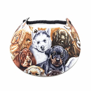 May include: A white visor with a black elastic band. The visor is covered in a colorful print of various dog breeds.