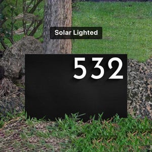May include: Black metal house number sign with white numbers "532" on a green lawn. The sign is solar lighted.