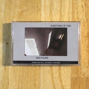 Puede incluir: Una cinta de cassette con el título del álbum "Something of Time" de Nightnoise. La portada presenta una imagen oscura y abstracta con luces y sombras. También se ve el texto "Windham Hill on BASF Chrome".