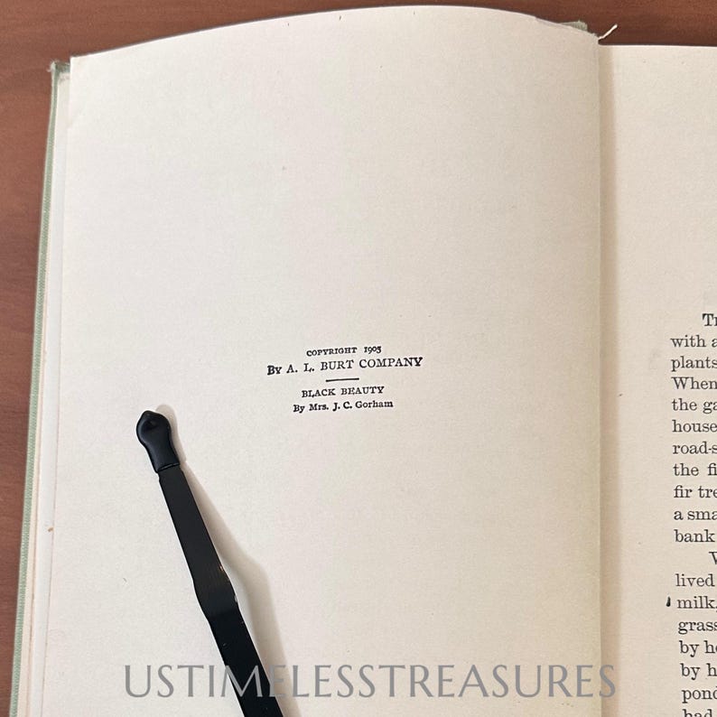 May include: Open book with text, including "BLACK BEAUTY" by Mrs. J. C. Gorham. A black bookmark is inserted. The book's copyright is 1905 by A. L. Burt Company. The bottom of the page has the text "USTIM LESSTREASURES".