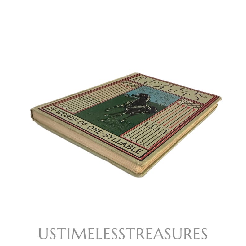 May include: A vintage hardcover book titled "Black Beauty" with the subtitle "In Words of One Syllable." The cover features a black horse on a green field with a blue sky. The book has a beige cover with red and green accents.