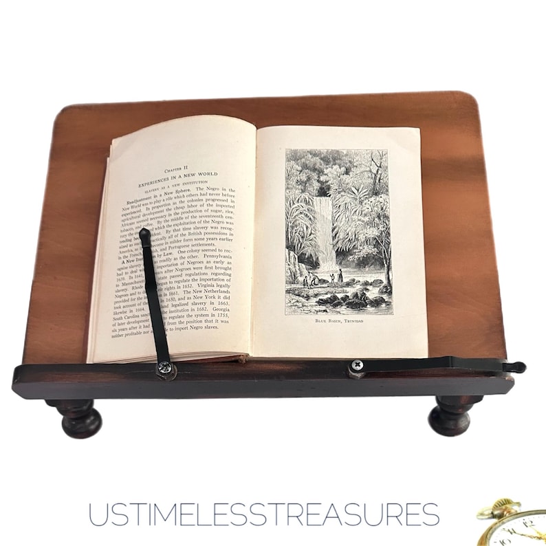 May include: A wooden book stand with a book open to a page with text and a black and white illustration of a waterfall. The stand is brown with a dark brown base and feet.