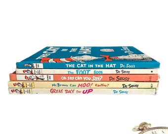 Puede incluir: Una pila de cuatro libros infantiles de Dr. Seuss, incluyendo "El Gato en el Sombrero", "El Libro del Pie", "Oh Say Can You Say?" y "Mr. Brown Can Moo! Can You?" Los libros están todos en buen estado y tienen cubiertas coloridas.