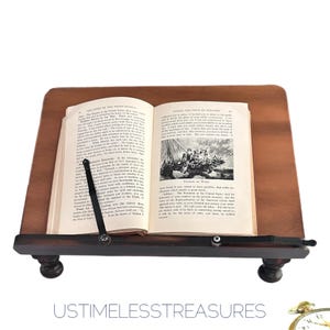 May include: A wooden book stand with a book open to a page with text and an illustration. The stand is dark brown with a sloped top and a lower shelf. The text "USTIMELESSTREASURES" is at the bottom.