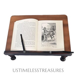 May include: A wooden book stand with a book open to a page with a horse illustration. The stand is dark brown with a slanted top and a lower shelf. The book is held in place by a black metal arm. The text "Black Beauty" is visible.