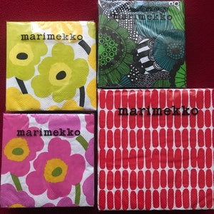 May include: Four packages of Marimekko brand paper napkins. The napkins feature floral and abstract patterns in various colors, including yellow, green, pink, and red. The Marimekko logo is printed on each package in black.