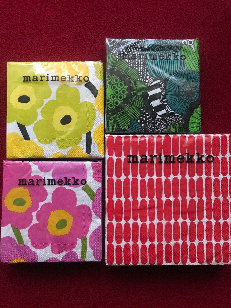 May include: Four packages of Marimekko brand paper napkins. The napkins feature floral and abstract patterns in various colors, including yellow, green, pink, and red. The Marimekko logo is printed on each package in black.