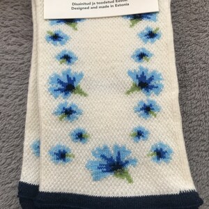 May include: A pair of white socks with a blue floral pattern. The socks have a navy blue cuff and the text "23-25 37-40 Disainitud ja tootedud Eestis. Designed and made in Estonia" is printed on the tag.