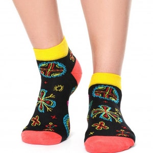 May include: A pair of black ankle socks with a colorful floral pattern. The socks have a yellow cuff and a red heel and toe.