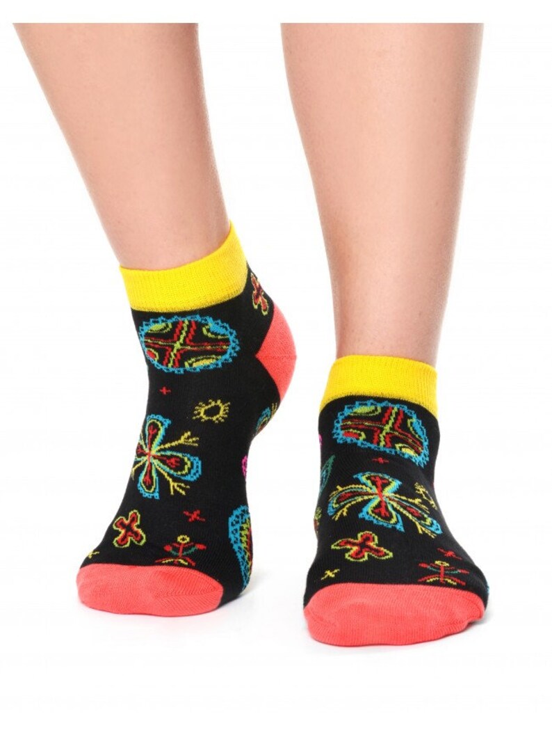 May include: A pair of black ankle socks with a colorful floral pattern. The socks have a yellow cuff and a red heel and toe.
