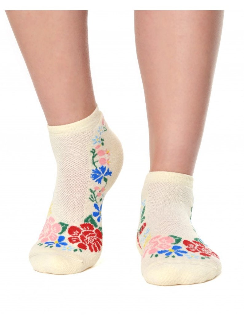 May include: A pair of cream-colored ankle socks with a floral design. The flowers are red, blue, pink, and yellow.