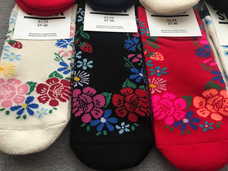 May include: Three pairs of socks with floral patterns. The socks are white, black, and red. The socks have a size tag that reads "23-25 37-40" and "Distributed ja tootundud Eesti. Designed and made in Estonia."