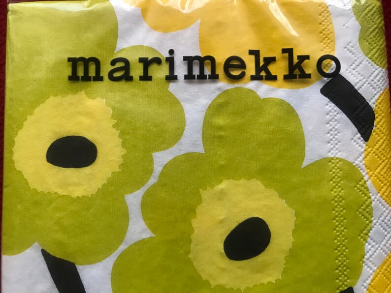 May include: A package of Marimekko brand paper napkins. The napkins feature a repeating floral pattern in shades of yellow and green on a white background. The word "marimekko" is printed in black block letters.