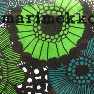 May include: Close-up of a patterned design featuring large, stylized floral shapes in green, teal, and black. The word "marimekko" is printed in black across the top of the image. The design is bold and graphic.