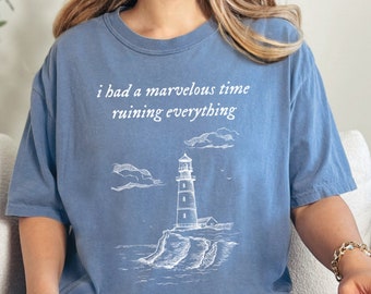 May include: A blue jean t-shirt with a white graphic of a lighthouse and the text "i had a marvelous time ruining everything".