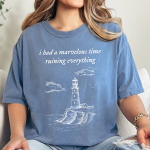 May include: A blue jean t-shirt with a white graphic of a lighthouse and the text "i had a marvellous time ruining everything".