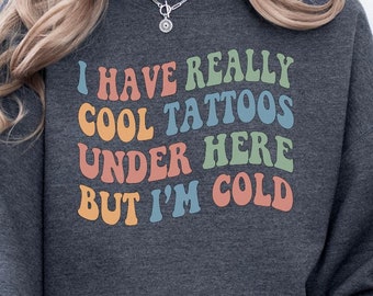 May include: A dark gray sweatshirt with the text "I have really cool tattoos under here but I'm cold" in rainbow colors.