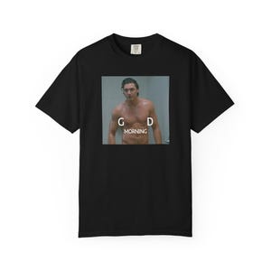 Può includere: T-shirt nera con un'immagine quadrata di un uomo sotto la doccia. L'immagine ha le lettere "G" e "D" su entrambi i lati della parola "MORNING" in testo bianco. La t-shirt è realizzata in un materiale morbido.