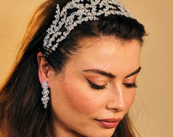May include: A silver headband with a delicate, intricate design of leaves and flowers, adorned with sparkling crystals. The headband is worn by a person with long, dark hair.