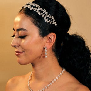 Op de afbeelding: Een bruidsjuwelenset met een delicate kristallen hoofdband, een ketting met een traanvormige hanger en bijpassende oorbellen. De juwelen zijn gemaakt van zilver en hebben een sprankelend kristallen ontwerp.