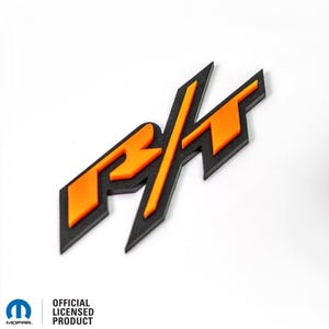 May include: A black and orange "R/T" emblem. The "R" and "T" are in orange with a black outline. The slash is black and angled.